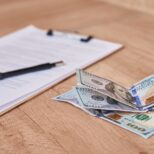 Document, pen and dollar bills on the table, close up