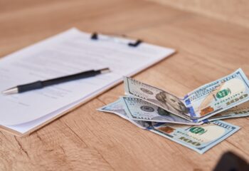 Document, pen and dollar bills on the table, close up